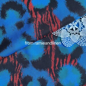 May include: Close-up of a blue and black fabric with a red and white abstract pattern. A white crocheted lace trim is visible at the top of the image. The text "from ramieandlinen" is visible in the center of the image.