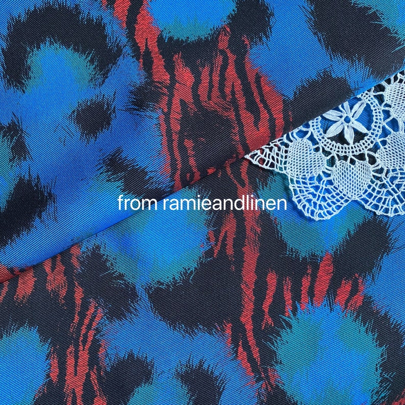 May include: Close-up of a blue and black fabric with a red and white abstract pattern. A white crocheted lace trim is visible at the top of the image. The text "from ramieandlinen" is visible in the center of the image.