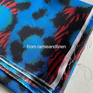 May include: Close-up of a folded fabric with a blue, black, red, and green abstract print. The fabric has a textured surface and is folded in thirds. The text "from ramieandlinen" is visible in the image.