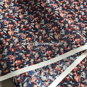 Pode incluir: Close-up de um tecido com fundo branco e um padrão repetitivo de formas abstratas vermelhas, azuis e pretas. O tecido tem uma borda branca.