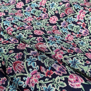 May include: A navy blue fabric with a floral pattern in shades of pink, purple, and green. The fabric has a subtle texture and a slightly sheen finish.