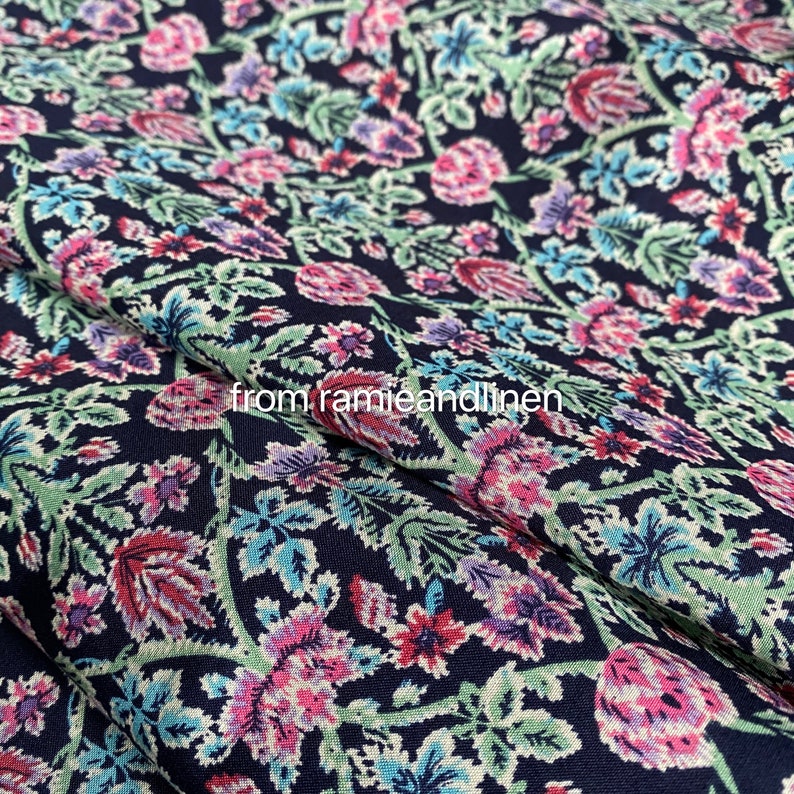 May include: A navy blue fabric with a floral pattern in shades of pink, purple, and green. The fabric has a subtle texture and a slightly sheen finish.