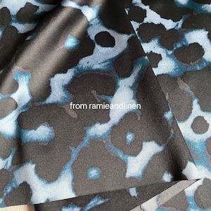 May include: Black satin fabric with a blue and white floral pattern. The fabric is folded over itself, showing the pattern on both sides. The text "from ramieandlinen" is printed on the fabric.