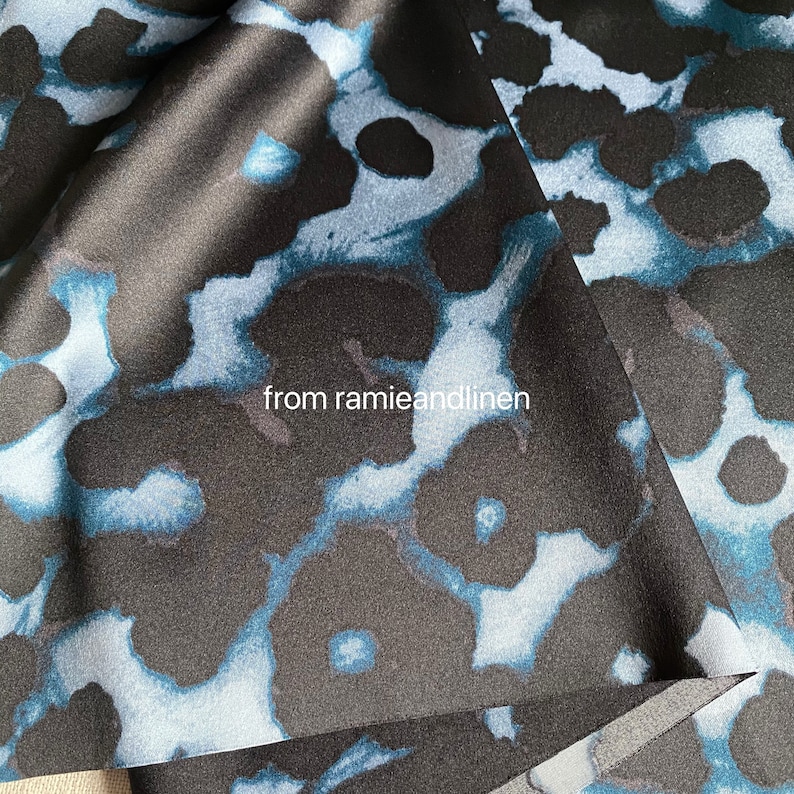 May include: Black satin fabric with a blue and white floral pattern. The fabric is folded over itself, showing the pattern on both sides. The text "from ramieandlinen" is printed on the fabric.