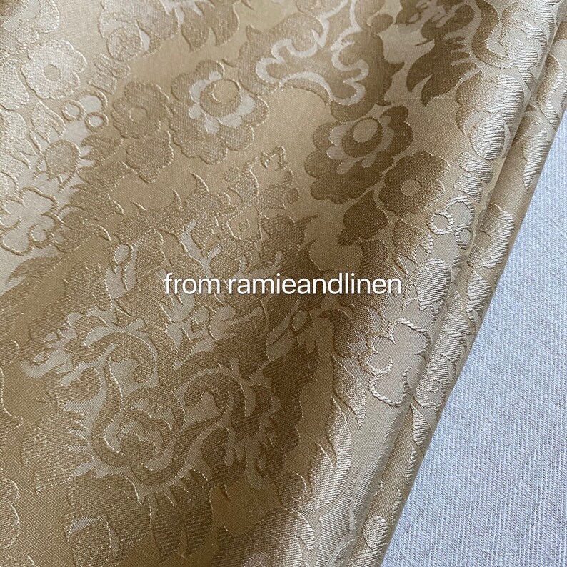 May include: A close-up of a gold fabric with a raised floral pattern. The fabric has a subtle sheen and a soft texture.