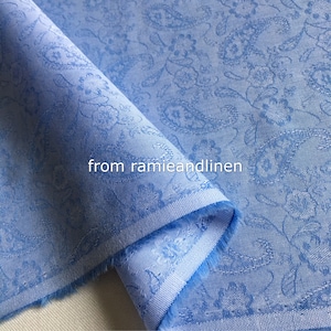 May include: A close-up of a light blue fabric with a white floral pattern. The fabric is folded in half and the edges are frayed.