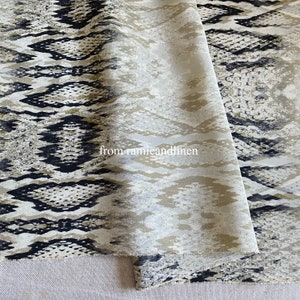 May include: A close-up of a beige fabric with a black and brown snake skin pattern. The fabric is folded in half and the text "from ramieandlinen" is visible in the centre of the image.