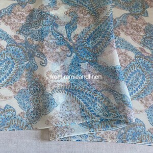Puede incluir: Una tela transparente con un patrón de paisley en tonos azules, marrones y blancos. La tela está doblada por la mitad, mostrando el patrón en ambos lados.