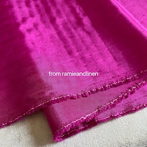Könnte beinhalten: Nahaufnahme eines leuchtend fuchsia-rosa Stoffes mit einem dezenten Glanz. Der Stoff hat eine rohe Kante und ist über sich selbst gefaltet. Der Text "from ramieandlinen" ist im unteren mittleren Bereich des Bildes sichtbar.