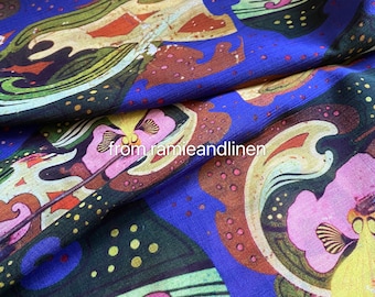Op de afbeelding: Een blauwe stof met een kleurrijke, abstracte print met draaiende patronen, bloemen en stippen. De stof heeft een textuur, geweven look.