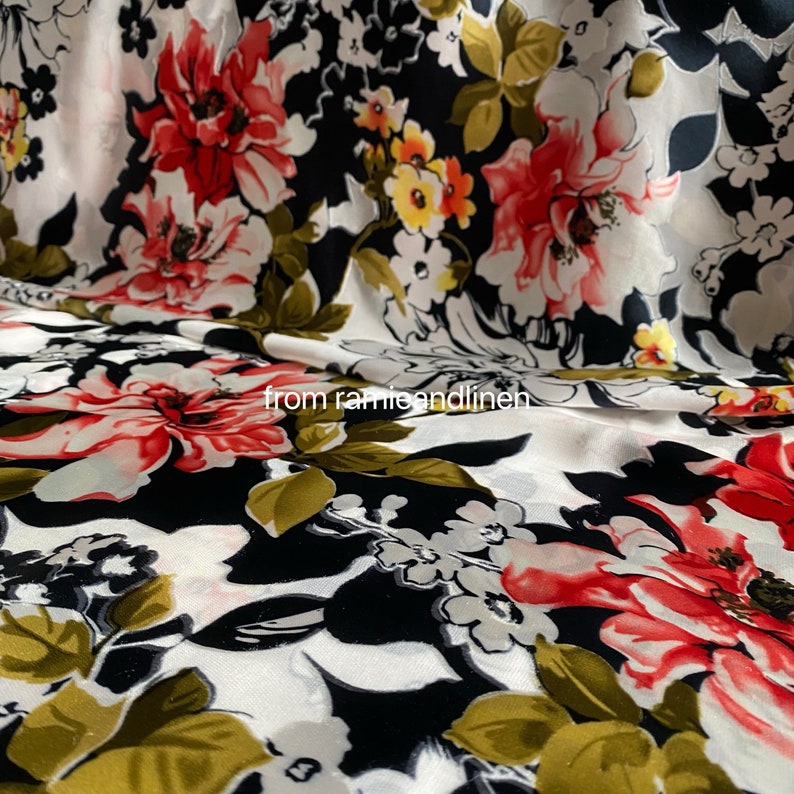 May include: White fabric with a black background and a large floral print in shades of red, white, and yellow. The fabric has a silky sheen and a soft texture.
