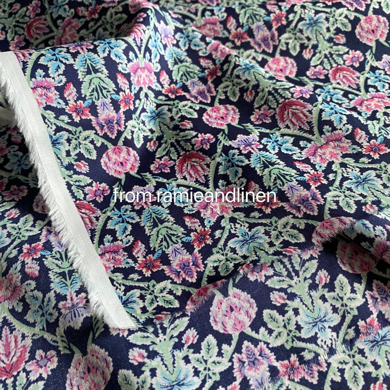 May include: A navy blue fabric with a floral pattern featuring pink, green, and blue flowers. The fabric has a subtle texture and a soft, flowing drape.