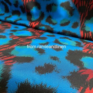 May include: Blue fabric with a black, red, and green leopard print. The fabric has a textured, woven look.