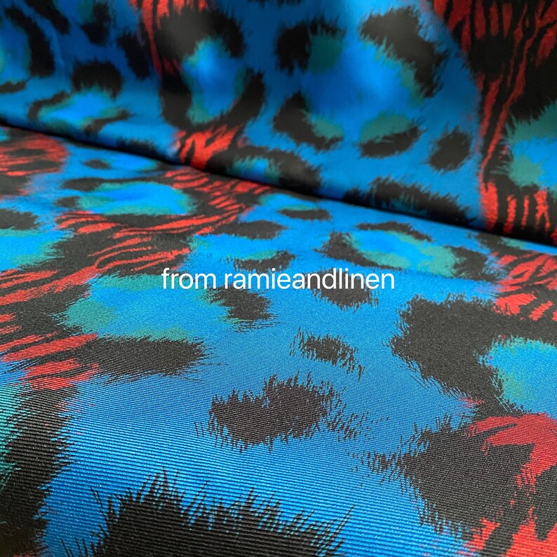 May include: Blue fabric with a black, red, and green leopard print. The fabric has a textured, woven look.