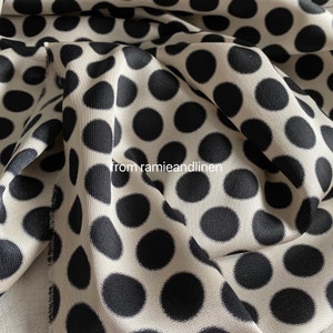 May include: Close-up of a white fabric with black polka dots. The fabric is folded and the polka dots are visible in the folds.