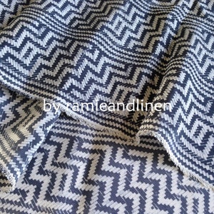 May include: Close-up of a fabric with a black and white chevron pattern. The fabric has a slightly textured surface and a raw edge.