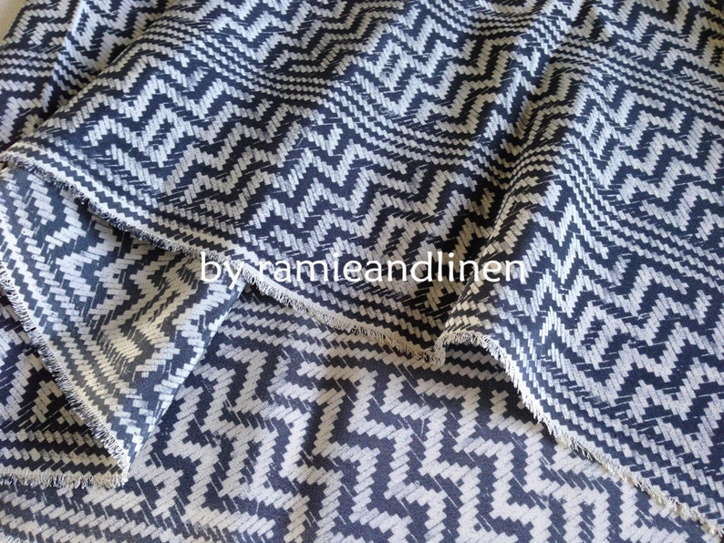 May include: Close-up of a fabric with a black and white chevron pattern. The fabric has a slightly textured surface and a raw edge.