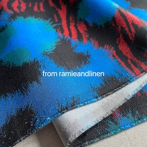 May include: Close-up of a blue, black, and red fabric with a brushstroke pattern. The fabric has a white lining and the text "from ramieandlinen" is visible.