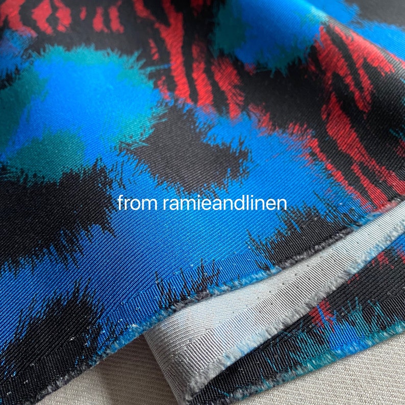 May include: Close-up of a blue, black, and red fabric with a brushstroke pattern. The fabric has a white lining and the text "from ramieandlinen" is visible.