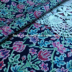 May include: A close-up of a dark blue fabric with a floral pattern. The fabric features pink, blue, and green flowers on a dark blue background. The fabric is folded in half and a white crocheted doily is partially visible in the top right corner. The text "from ramieandlinen's etsy shop" is visible in the lower left corner.