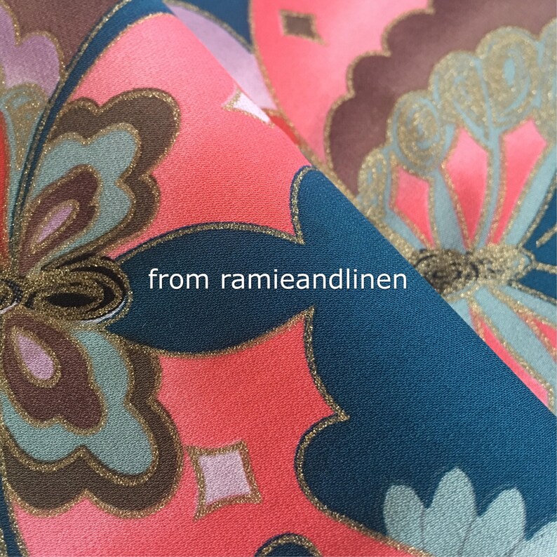 K&ouml;nnte beinhalten: Nahaufnahme eines blaugr&uuml;nen Stoffes mit einem rosa und goldenen Schmetterlingsmuster. Der Stoff hat einen dezenten Schimmer und ist perfekt f&uuml;r Bastel- oder N&auml;hprojekte.