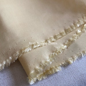 May include: Close-up of a pale yellow fabric with a fringed edge. The fabric has a subtle texture and a dotted pattern. The text "from ramieandlinen" is visible in the lower right corner.