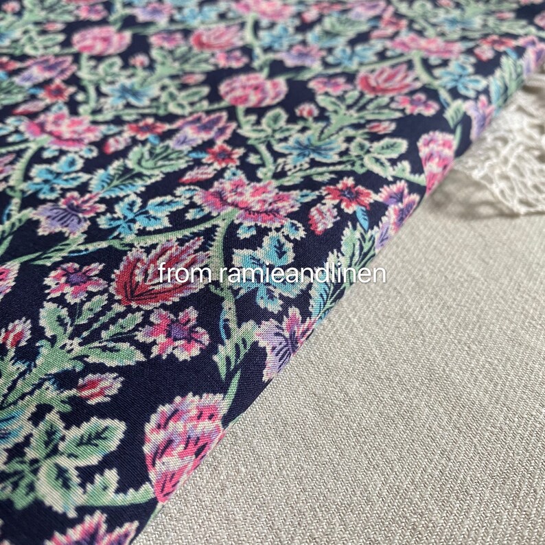 May include: A close-up of a dark blue fabric with a floral pattern in shades of pink, green, and blue. The fabric is folded over and the text "from ramieandlinen" is visible in the lower right corner.