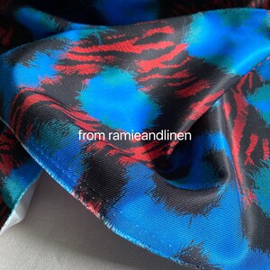 May include: Close-up of a blue, red, and black fabric with a brushstroke pattern. The fabric has a subtle texture and a slightly shiny finish.