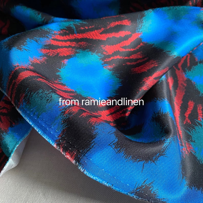 May include: Close-up of a blue, red, and black fabric with a brushstroke pattern. The fabric has a subtle texture and a slightly shiny finish.
