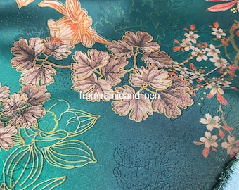 May include: Green fabric with a floral pattern featuring brown leaves, gold accents, and white flowers. The fabric has a subtle texture.