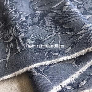 May include: Close-up of a dark grey fabric with a white floral pattern. The fabric has a raw edge and the text "from ramieandlinen" is visible.