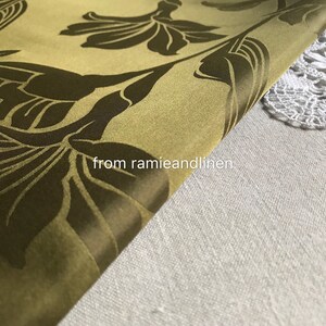 Op de afbeelding: Een close-up van een groene stof met een donkerbruin bloemenpatroon. De stof is dubbelgevouwen en de tekst "from ramieandlinen" is zichtbaar in de rechterbenedenhoek.