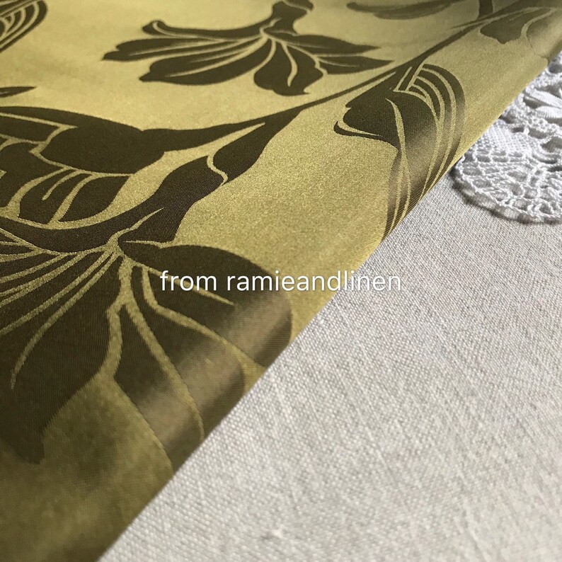 Op de afbeelding: Een close-up van een groene stof met een donkerbruin bloemenpatroon. De stof is dubbelgevouwen en de tekst "from ramieandlinen" is zichtbaar in de rechterbenedenhoek.