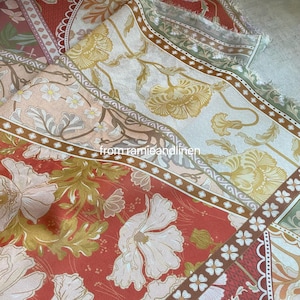 Op de afbeelding: Close-up van bloemenstof in tinten rood, perzik en crème. De stof heeft grote bloemen- en bladerpatronen met een randontwerp. De tekst "from ramieandlinen" is zichtbaar.