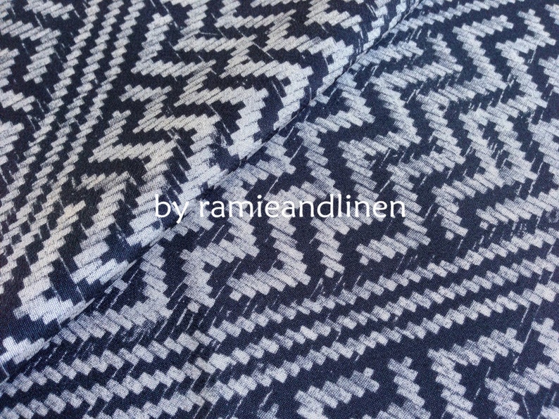 May include: A close-up of a dark blue and white patterned fabric with a geometric design. The fabric is soft and has a subtle sheen.