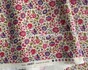 May include: A close-up of a white fabric with a floral pattern. The fabric features small pink, red, and purple flowers on a white background. The fabric is labeled "Liberty Printed in Japan".