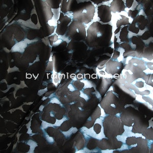 May include: Black fabric with a blue and white abstract animal print pattern. The fabric is smooth and silky.
