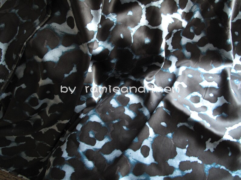 May include: Black fabric with a blue and white abstract animal print pattern. The fabric is smooth and silky.