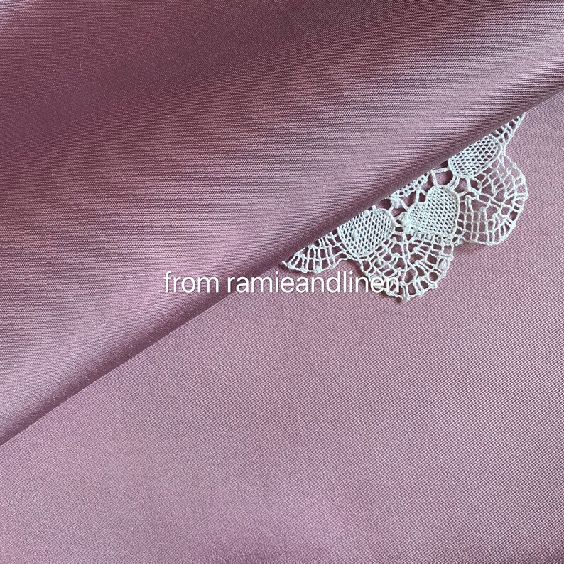 May include: A close-up of a mauve fabric with a white lace overlay. The lace has a delicate heart pattern. The text "from ramieandlinen" is visible in the lower left corner.