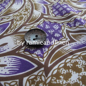May include: A close-up of a brown and purple fabric with a white button in the center. The fabric has a repeating pattern of paisley-like shapes. The button is silver and has a decorative design.