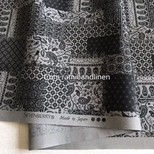 May include: Black and white paisley patterned fabric with a patchwork design. The fabric has a textured surface and is made in Japan. The label reads "SEVENBERRY® Made by Japan".