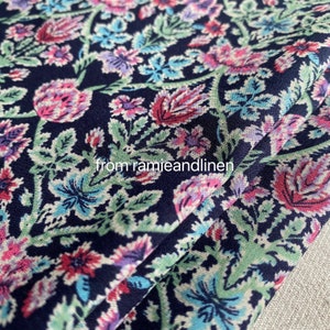 May include: A close-up of a dark blue fabric with a floral pattern. The pattern features pink, blue, and green flowers on a dark blue background. The fabric is folded in half, and the edge of the fold is visible.