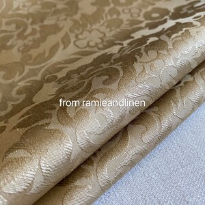 May include: A close-up of a gold fabric with a damask pattern. The fabric is folded in half and has a soft, luxurious feel.