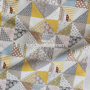 May include: A fabric with a patchwork design featuring a variety of geometric shapes and patterns in shades of yellow, grey, brown, and blue. The fabric is made up of small squares and triangles, each with a different pattern. The fabric is perfect for quilting, sewing, and other craft projects.