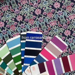 May include: A color chart with various shades of blue, green, purple, and pink. The chart is labeled with RAL color codes and names in German. The chart is on a dark blue fabric with a floral pattern.