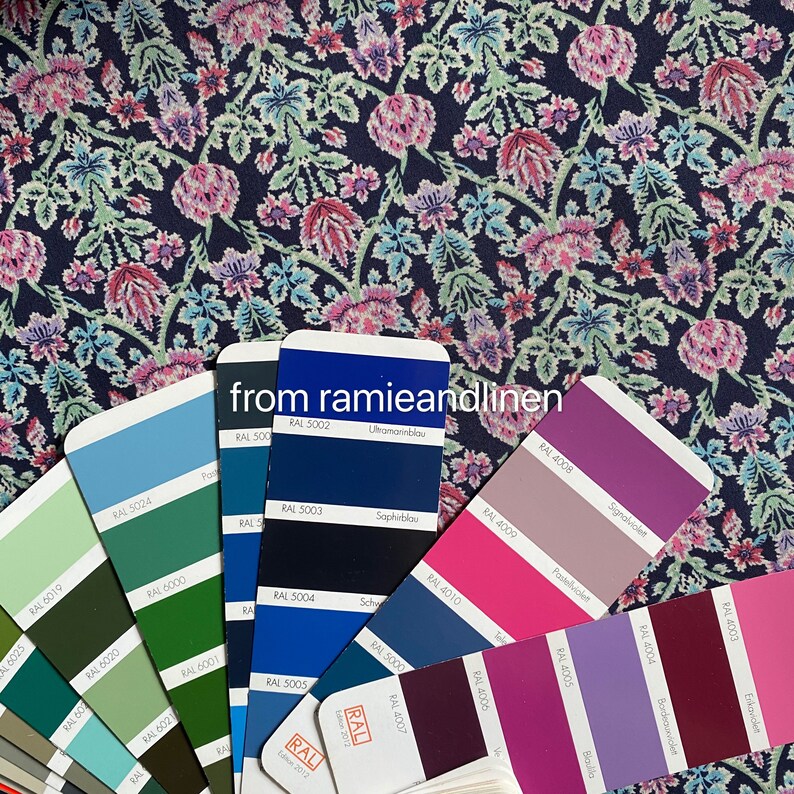 May include: A color chart with various shades of blue, green, purple, and pink. The chart is labeled with RAL color codes and names in German. The chart is on a dark blue fabric with a floral pattern.