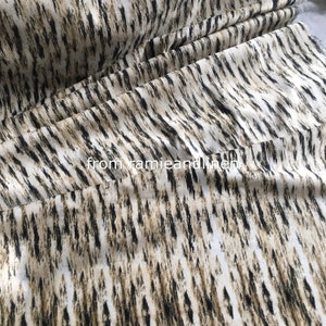 Könnte beinhalten: Nahaufnahme eines weißen Stoffes mit einem abstrakten Druck in Schwarz und Braun. Der Stoff hat eine weiche, strukturierte Haptik und ist perfekt für Polster oder Kleidung.