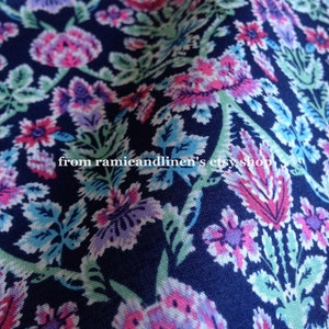 May include: A close-up of a navy blue fabric with a floral pattern. The pattern features pink, purple, and green flowers on a dark blue background. The fabric is soft and has a subtle sheen.