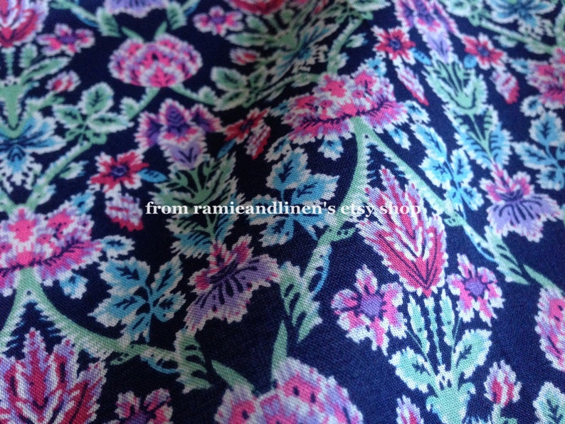 May include: A close-up of a navy blue fabric with a floral pattern. The pattern features pink, purple, and green flowers on a dark blue background. The fabric is soft and has a subtle sheen.