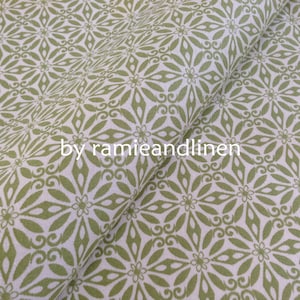 May include: Green and white fabric with a repeating pattern of stylized flowers. The fabric is folded in half, and the text "by ramieandlinen" is visible in the center of the image.